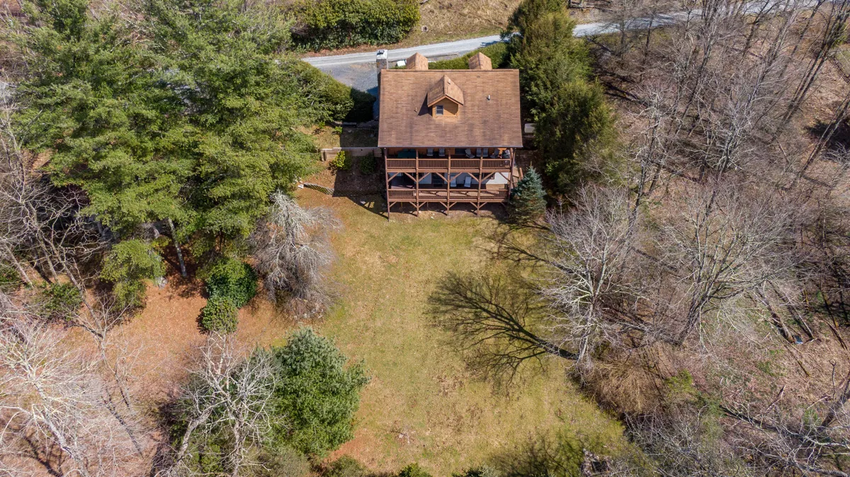 This image presents a wide view of the house, the driveway, and surrounding greenery. The driveway is clearly visible, providing a sense of ample parking and easy access. The home’s position on a gentle slope emphasizes its mountain perch, while the verdant landscape hints at proximity to trails and the outdoors.