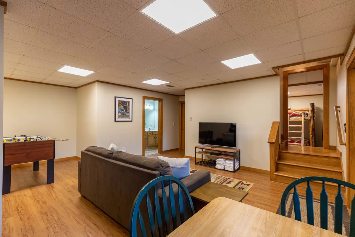 This interior scene showcases a cozy game room featuring a sofa, a television perfect for movie nights, a foosball table for friendly tournaments, and a dining table for gathering. The room exudes a relaxed, sociable vibe, highlighting spaces where guests can unwind together.