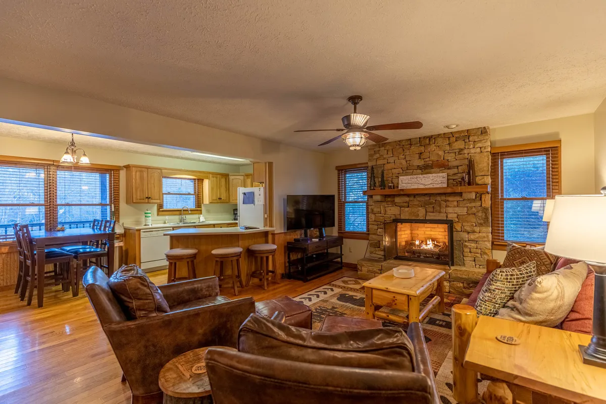 This image captures the heart of the main living space, prominently featuring a cozy gas fireplace, plush seating area, a visible dining table, and the seamless connection to the kitchen. The scene is filled with warmth and suggests a space perfect for family gatherings, movie nights, and cozy evenings by the fire.