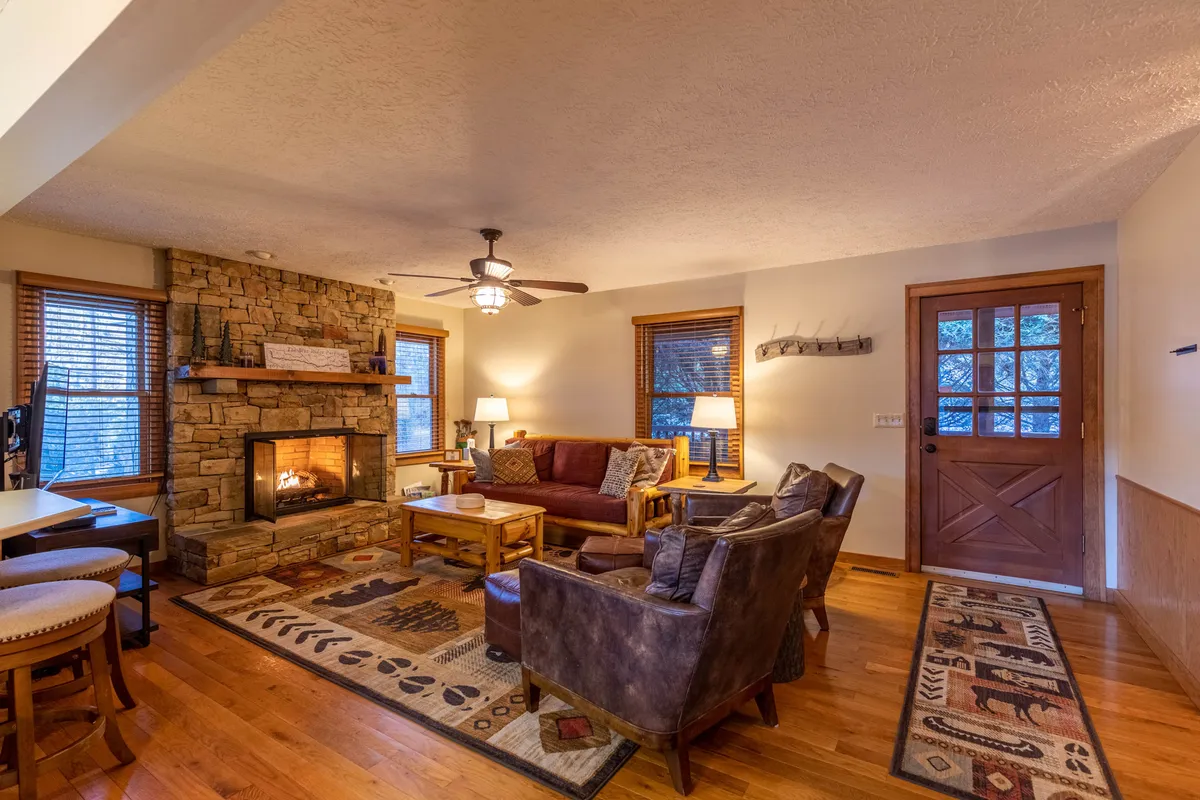 The image showcases a cozy living room with a rustic stone fireplace as the focal point, surrounded by plush, comfortable seating and a wooden coffee table. Soft lighting creates a warm, welcoming atmosphere, perfect for gathering with friends or family. The space invites relaxation, conversation, and enjoying a mug of hot cocoa by the fire after a day exploring the Appalachian Ski Mountain.
