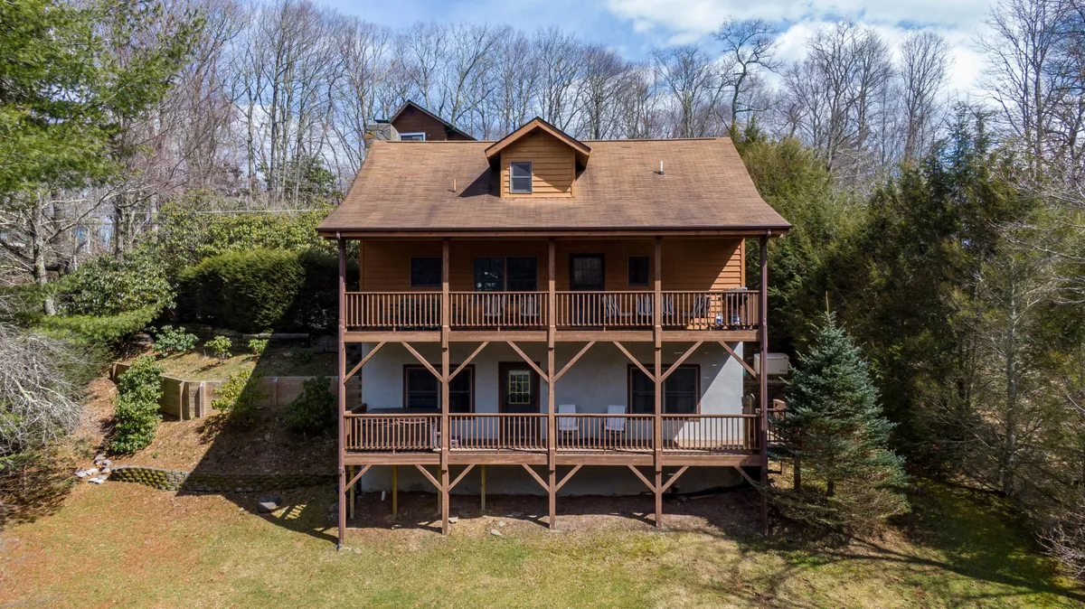 A wide shot of a two-story wooden cabin with a spacious balcony, nestled among natural surroundings. The balcony offers scenic views, and the overall scene captures the cabin’s proximity to nature and the ski area.