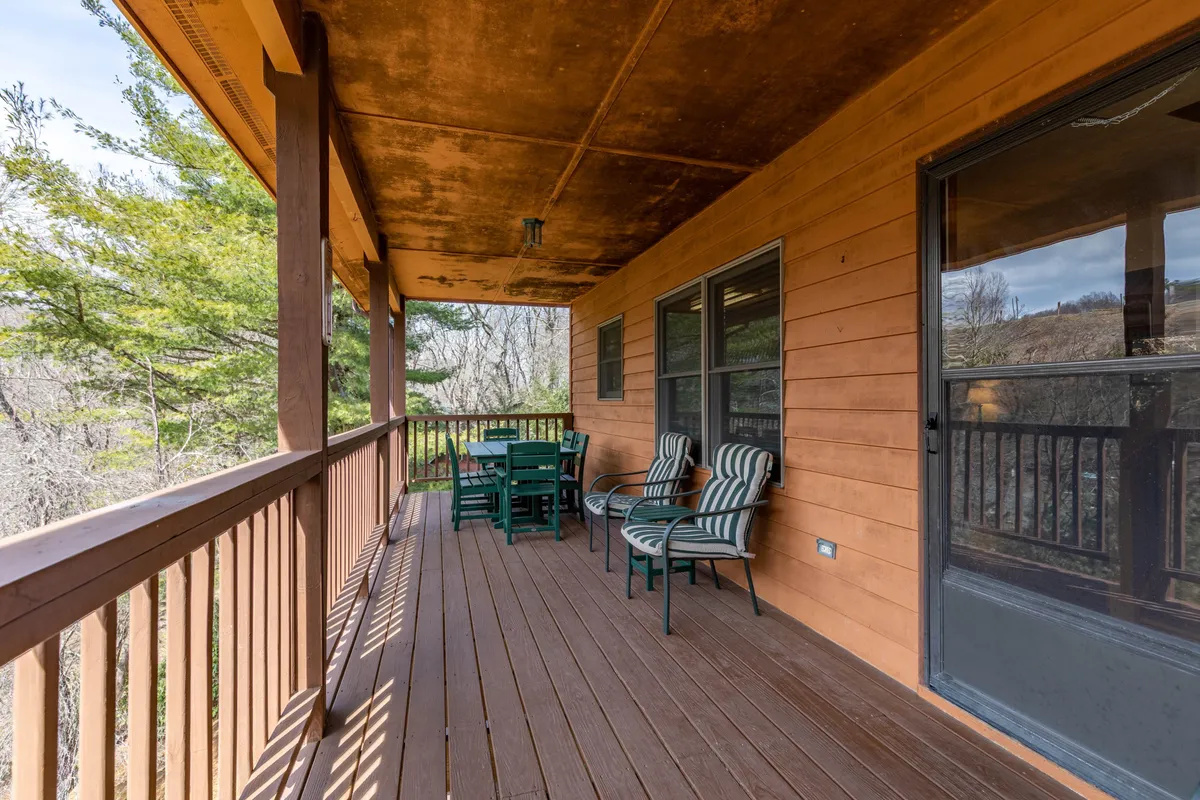 This image captures a spacious wooden deck outfitted with green and striped lounge chairs, surrounded by wooden railings and open to the natural mountain air. The deck invites relaxation and socializing, with views into the surrounding landscape that hint at the mountain retreat setting.