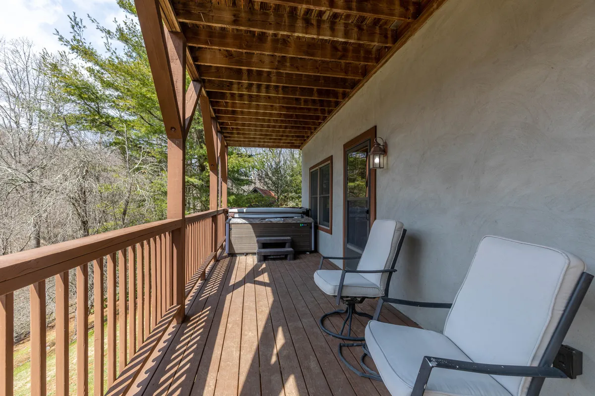 A cozy exterior setting featuring a bubbling hot tub and rocking chairs on a wooden deck, surrounded by mountain views and nature. This inviting outdoor space hints at relaxation after a day of adventure.
