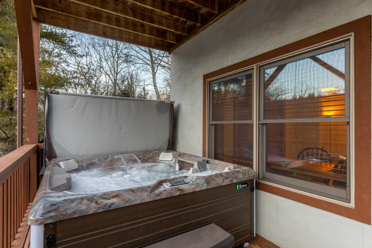 An exterior shot focusing on a private hot tub nestled among trees, with windows reflecting the peaceful outdoor ambiance. The setting is tranquil, inviting guests to unwind and relax after an action-packed day.