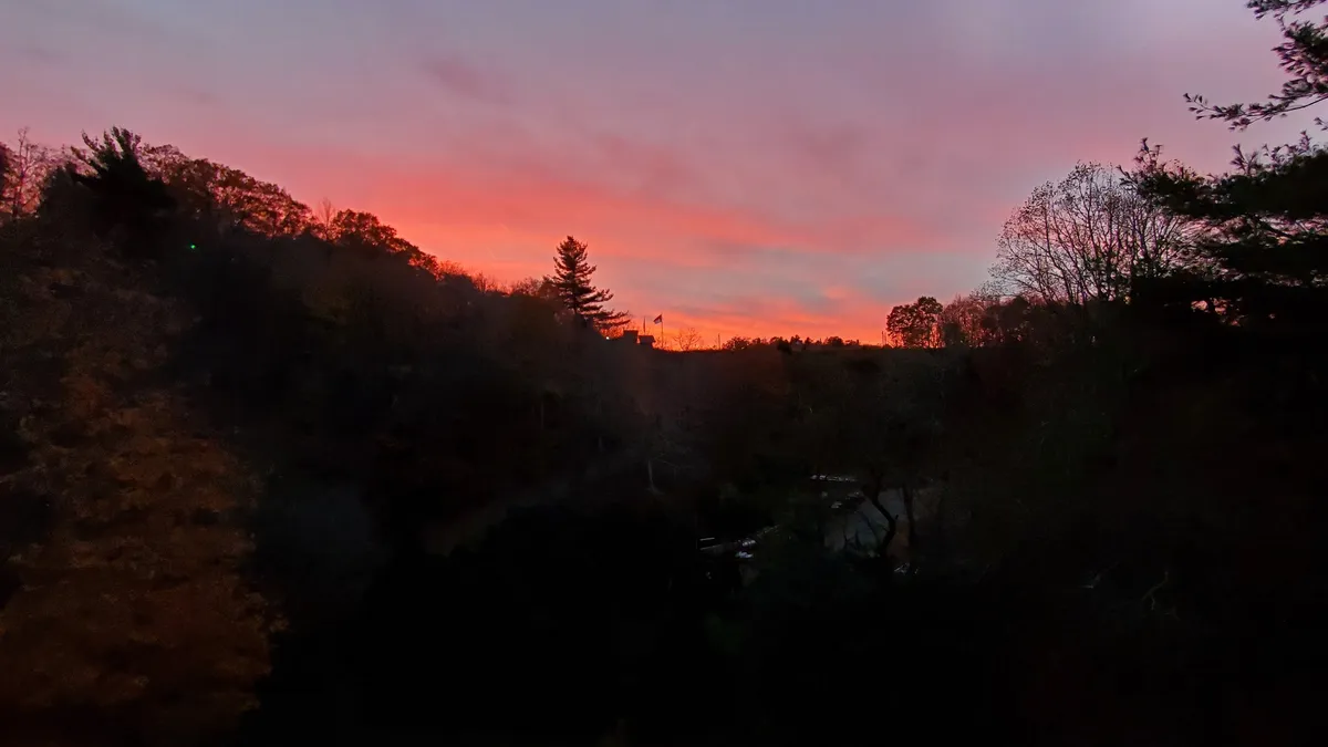 A breathtaking view of the vibrant sunset sky above silhouetted trees and the horizon, evoking the tranquility and beauty of the mountain surroundings. This scenic shot captures the peaceful allure of evenings spent in nature.